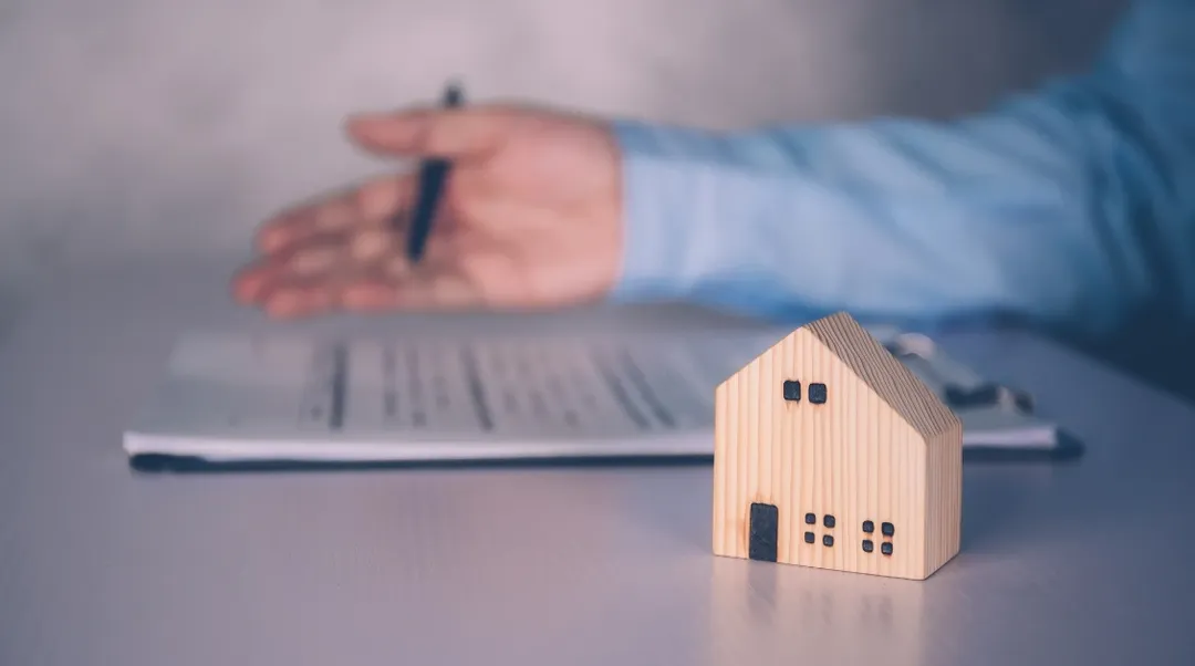 Kleines Holzhaus vor Mietvertragsunterlagen und Stift