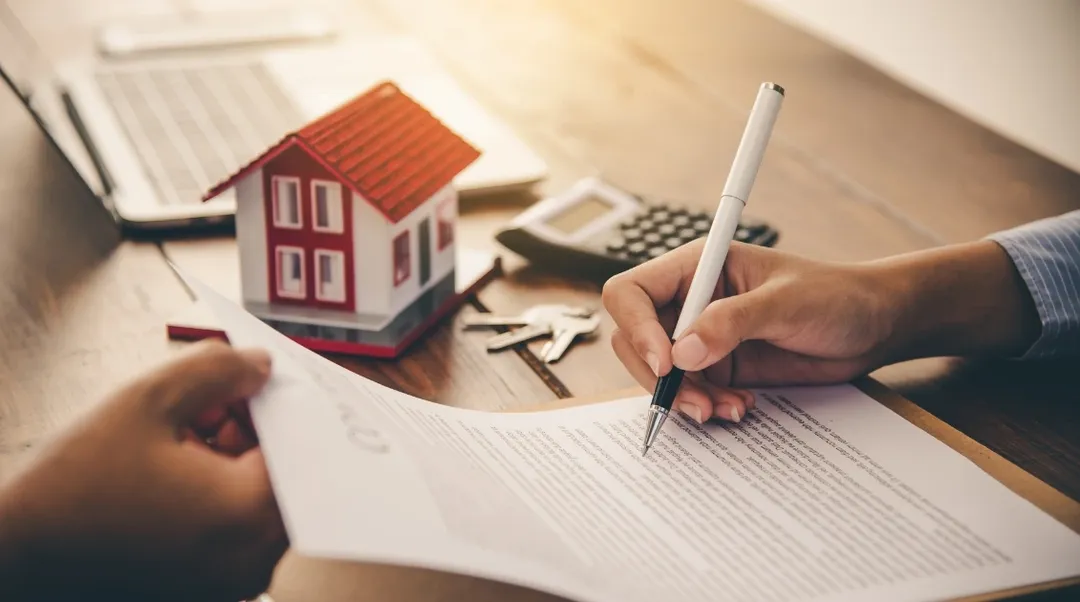 Unterschrift unter Mietvertrag mit Miniaturhaus und Schlüssel